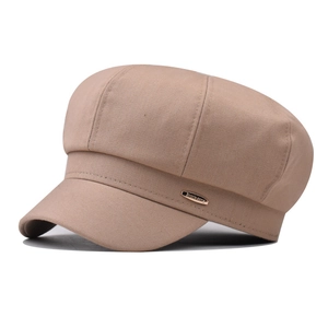 Detail of beige newsboy cap showing twill fabric texture and golden logo plate
