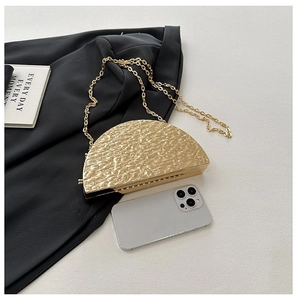 Detailed view of gold semi-circle evening bag featuring hammered texture and metal chain