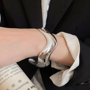 Close-up of a wide silver wavy cuff bracelet worn with a black suit for a modern look