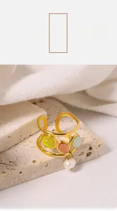 Detail of a triple-layered gold wave ring with colored gemstones and a hanging white pearl