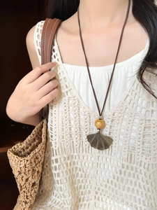 Detail of wooden bead and ginkgo leaf pendant on a boho style sweater chain necklace