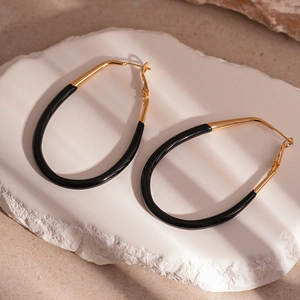 Detail view of large gold and black enamel oval drop earrings on a stone textured background