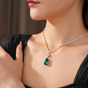 Close-up of gold tennis necklace featuring emerald water drop pendant on a model