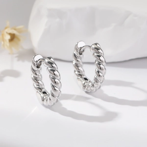 Macro shot of silver twisted rope hoop earrings on a minimalist white stone background