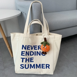 Canvas tote bag with blue lettering and orange persimmon plush charm on a grey sofa
