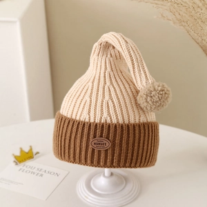 Detail of baby winter knit hat with pompom and leather tag on a white stand
