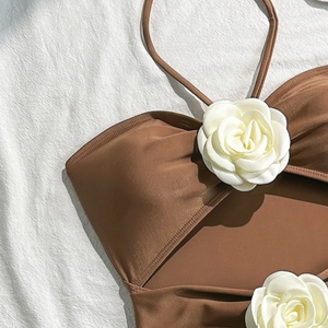 Detailed view of the brown swimsuit with a white camellia flower and halter neckline