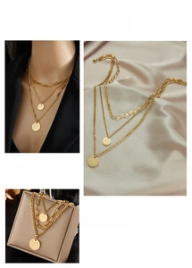 Close-up of triple-layered gold necklaces with engraved round pendants on a silk background