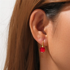 Detailed view of red cushion cut gemstone drop earring on model ear with gold hooks