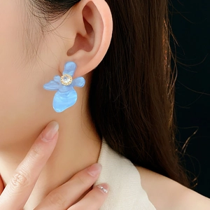 Détail d'une boucle d'oreille fleur en résine bleue avec zircon portée par un mannequin