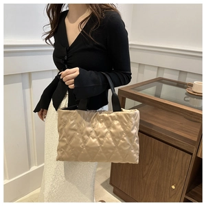 Detail of beige quilted tote bag with black handles showing puffer texture and capacity