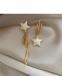 Detail of asymmetric gold-plated star earrings with mother-of-pearl and tassel chain