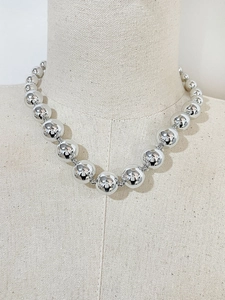 Detailed view of silver metallic bead necklace on a minimalist fabric bust display
