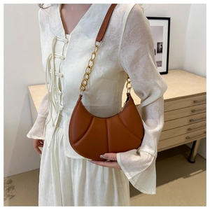 Close-up of brown pleated crescent bag featuring golden chain and leather strap