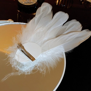 Detailed view of elegant white feather hair clip with metal duckbill clasp on a mirror