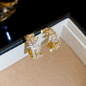 Macro shot of gold C-shaped irregular earrings with sparkling rectangular zircon stones