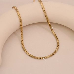 Layered gold herringbone snake chain necklace displayed on a beige circular jewelry stand