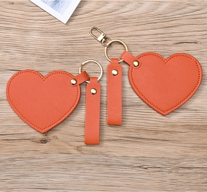 Close-up of two heart-shaped orange leather keychains with gold hardware on wood
