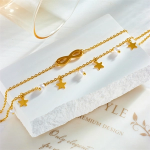 Double-layered golden infinity bracelet with star charms and pearls on marble