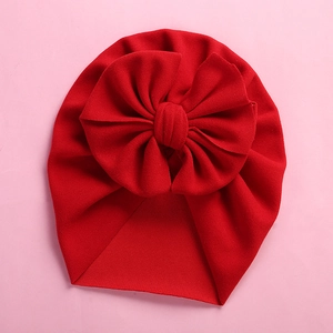 Detail of red baby turban hat with a large soft bow on a pink minimalist background