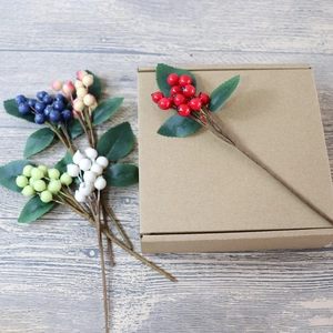 Close-up of five colorful artificial berry stems with green leaves for DIY home decor