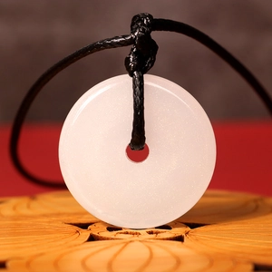 Detailed close-up of a white Ping'an Kou jade pendant on a carved wood base stand