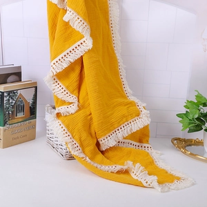 Yellow muslin baby blanket with white tassel fringe in a cozy home setting decor