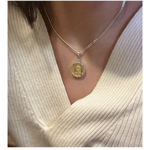 Detail of silver chain and two-tone coin pendant with portrait relief on white sweater
