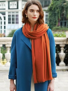 Detail of orange cashmere-like scarf showing soft texture and tassels on a model