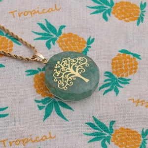 Detail showing green faceted stone pendant with golden tree of life on twist chain