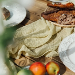 Close-up of beige wrinkled cheesecloth table runner texture on a rustic wooden table