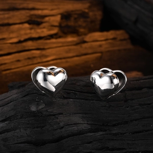 Polished silver 3D heart stud earrings presented on a dark textured wooden base