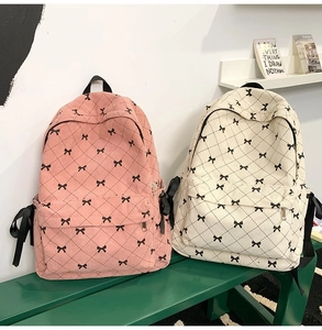 Pink and beige corduroy backpacks with diamond quilting and bow details on a green bench