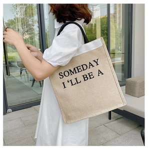 Detail of linen tote bag featuring 'SOMEDAY I'LL BE A' print and black tubular handles