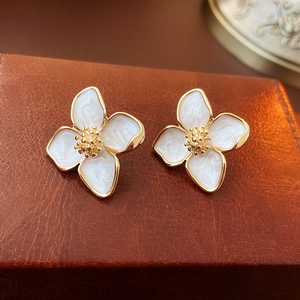 Détail de boucles d'oreilles fleur plaquées or avec pétales blancs sur boîte en cuir