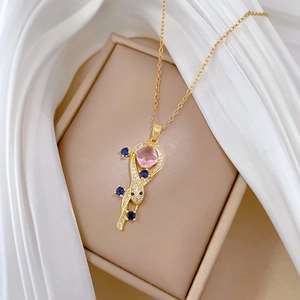 Detailed shot of golden snake necklace with pink gemstone pendant on beige jewelry box