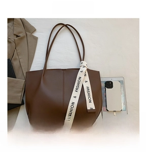 Macro view of a large dark brown tote bag with woven ribbon and office accessories