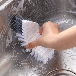 Flexible white cleaning brush scrubbing a stainless steel sink with soapy foam