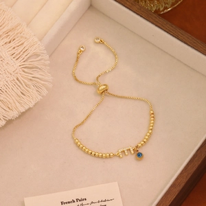 Dettaglio del bracciale dorato regolabile con occhio del diavolo e pendente lettera E