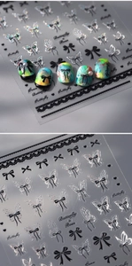 Close-up of holographic butterfly and black bow nail decals with 3D embossed texture