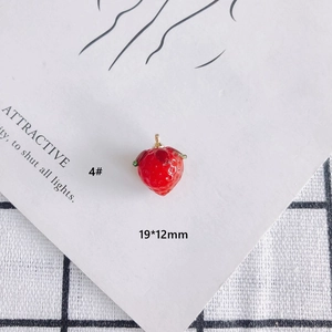 Close-up of red strawberry glass pendant with green leaves and golden metal ring