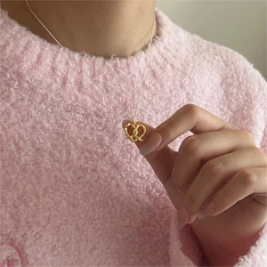 Close-up of a 925 sterling silver necklace with gold bow pendant on a pink sweater background
