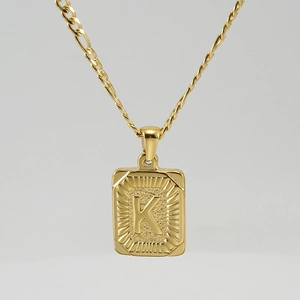 Macro shot of 18K gold plated square pendant featuring embossed letter K and figaro chain