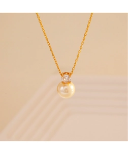 Macro detail of elegant gold-plated snake chain featuring a pearl and zircon pendant