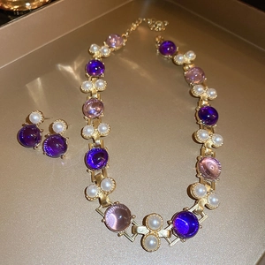 Détail d'une parure vintage avec pierres violettes et perles blanches sur un plateau