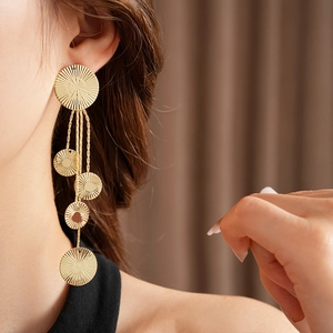 Close-up of golden multi-disc tassel earrings with radial texture on a model