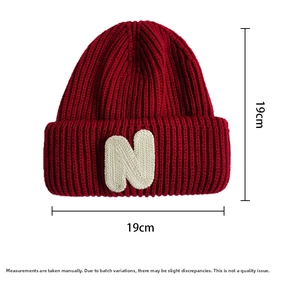 Detail view of a dark red knit beanie with a plush white N patch and 19x19cm dimensions