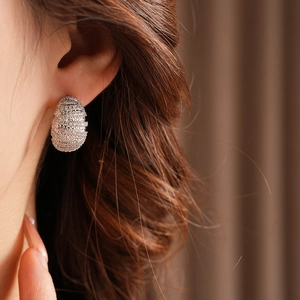 Close-up of silver earrings with pave-set crystals and a textured spiral oval design