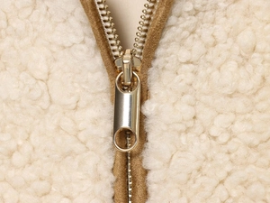 Detailed macro view of gold metal zipper on beige fleece fabric with brown piping
