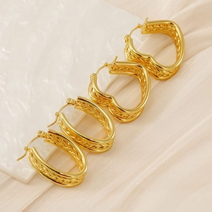 Macro detail of four gold twisted hoop earrings on silk fabric and marble background